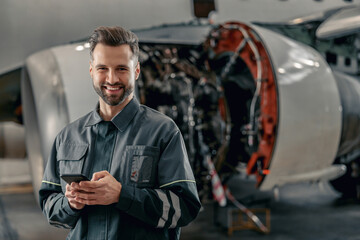 Joyful bearded man aircraft maintenance technician looking at camera and smiling while holding...