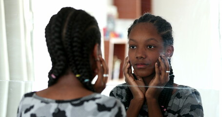 Teenager black girl looking at herself in mirror. Adolescent african girl inspecting face
