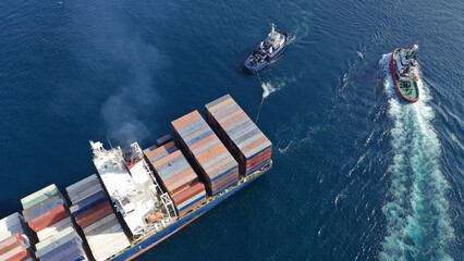 Aerial drone top down photo of tow - tug boat assisting by pulling or pushing container ship to...