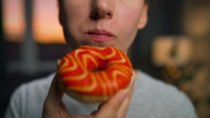 Sweet addiction concept. Woman eats orange donut closeup