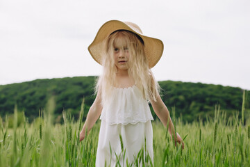 Adorable little girl playing in the wheat field on a warm summer day