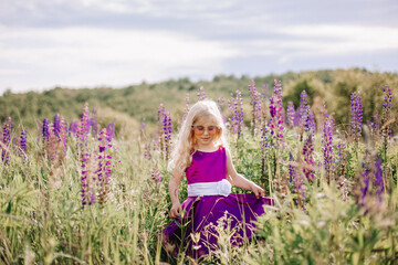 The girl in the hat walks in a field of lupines.