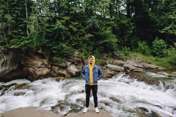 Fototapeta premium Happy male tourist standing outdoors in the forest near the mountain river.
