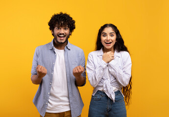 Wow, yes. Portrait of overjoyed indian man and woman cheering and shaking clenched fists looking at...