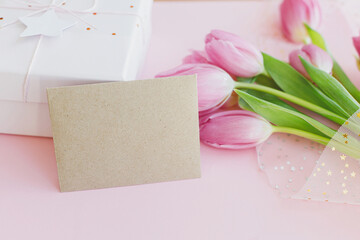 Empty greeting card, pink tulips bouquet and gift box on pink background. Greeting card template with space for text. Happy womens day. Happy Mothers day. 8 march