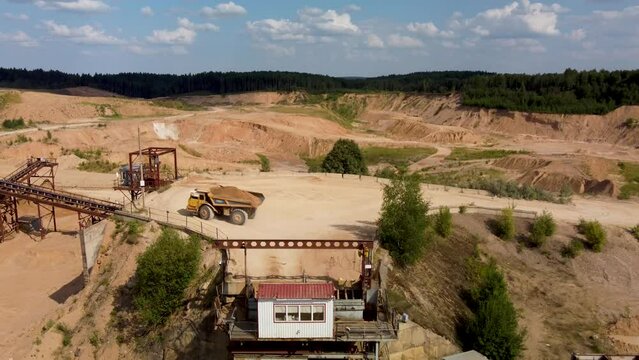 Loaded with sand yellow belaz truck  turns around on a base to unload sand on sunny day.
