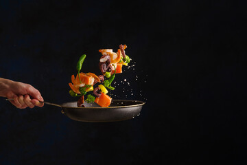 Assorted seafood in a frying pan in a state of levitation on a black background. The concept is cooking seafood, restaurant cuisine recipes. Hotel, restaurant, recipe book.