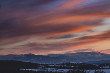 colorful sunset clouds over the countryside in czech republic with snow and mountains in the background on a winter day