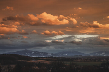 colorful sunset clouds over the countryside in czech republic with snow and mountains in the background on a winter day