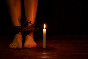 children's legs are tied with a rope in the dark near a candle, prison and slavery