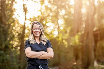 A medical professional with black scrubs with long hair outside in a natural background with copy space