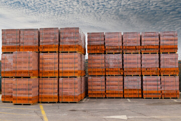 Red brick packed in stacks are stored on ground outdoors at a hardware store warehouse. Building bricks on pallets on an outdoor warehouse.