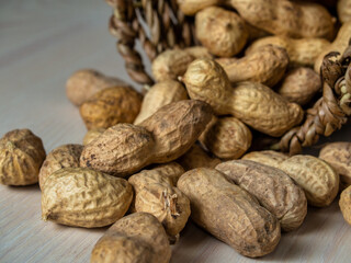 Shelled peanuts in a small wicker basket on a white background. Peanuts full from a wicker basket. Peanuts spill out of a wicker basket.