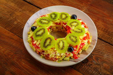 Puff salad with chicken breast and tomatoes, garnished with kiwi in a beige plate on a wooden table.