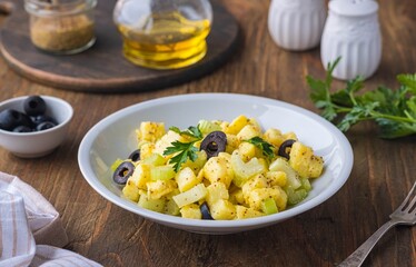 Potato salad with green selery and olives in a gray ceramic bowl on a wooden background. Recipes...
