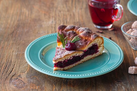 Sliced round yeast dough pie with cherries on a green ceramic plate on a brown wooden background.