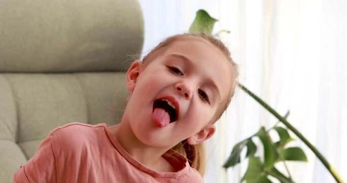 Child girl opens her mouth wide and teases. child shows her teeth and mouth. Mouth is wide open, tongue is stuck out as far as possible, with clear view of tongue
