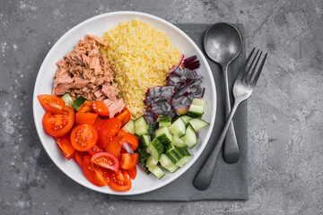 Food dieting concept, tuna salad. Couscous salad with conserved tuna, tomatoes, cucumbers and purple onions on table. Copy space.