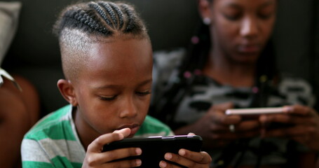 African siblings using cellphone at home. Black ethnicity children watching video on cellphone