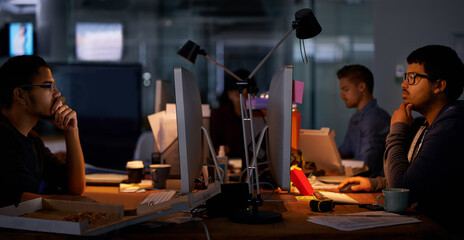 Getting the job done. Cropped shot of a group of young coworkers working in a dimly-lit office.