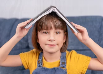 Rolgordijnen klein meisje met een boek onder haar hoofd en glimlacht © Albert Ziganshin