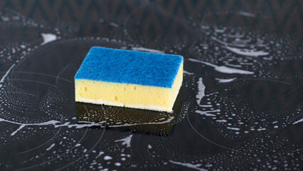 Yellow sponge on the stove in the foam. General cleaning concept.