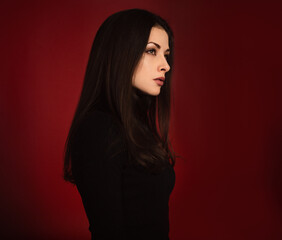 Beautiful confident serious business woman in black sweater posing with hand under the face on dark red background with empty copy space. Closeup profile