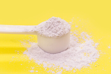 measuring spoon with casein or caffeine powder, food supplement, vitamin used by athletes, yellow background