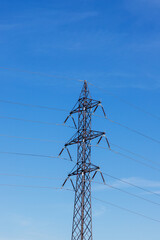 High voltage poles for electricity distribution in the countryside. In the background is a blue sky with dramatic clouds.