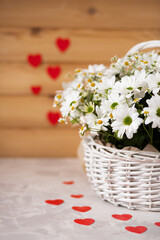 Fototapeta na wymiar Beautiful composition of summer daisies in a festive wicker basket for a birthday or anniversary, national women's day, March 8, mother's day. Red heart on background