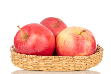 Three sweet organic, red apples in a plate of straw, macro, isolated on a white background.

