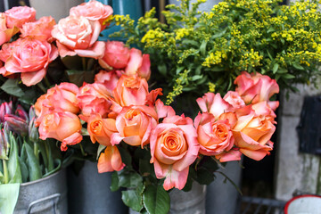 Bouquets of orange-pink roses on a background of yellow mimosa bouquets for sale in a store
