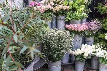 Fototapeta na wymiar White and pink roses, daisies, buttercups, gypsophila, eucalyptus, hydrangea, spruce, green parrot tulips are for sale at the entrance to the flower shop
