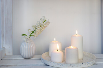 A white hyacinth in a 1970s fluted vase next to a tray of four lit candles is on the shelf. Minimalism. Scandinavian style.
