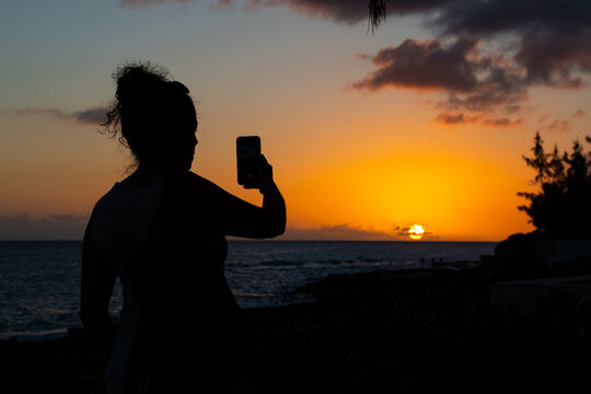 A young lady captures the setting sun on her camera phone so she can upload the image to her personal social media accounts
