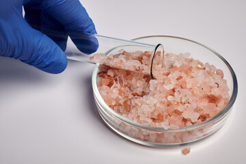 Hand takes rose salt from a Petri dish with a test-tube. Pink salt crystals in glass Petri Dish....