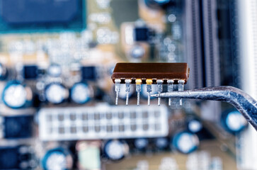 Microcircuit in tweezers on the background of the motherboard