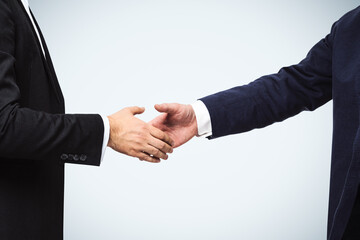 Two businessmen shake hands on a white wall background, deal concept, close up