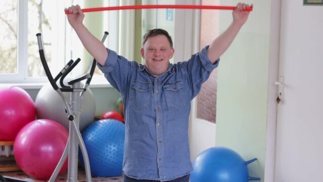 Portrait of a cheerful disabled man with Down syndrome doing sports exercises in the gym. Healthy lifestyle.