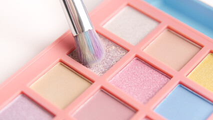 Make-up artist picks up pink pigment from bright colorful eyeshadow palette with a brush....