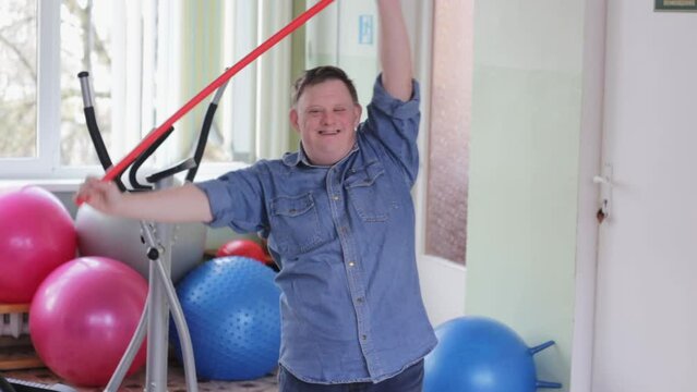 Portrait of a cheerful disabled man with Down syndrome doing sports exercises in the gym. Healthy lifestyle.