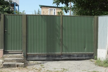 Fototapeta na wymiar one big green closed metal gate and door on a rural street