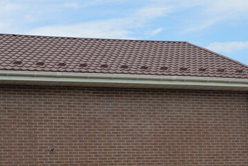 part of a big house from a brown brick wall under a tiled roof against a blue sky