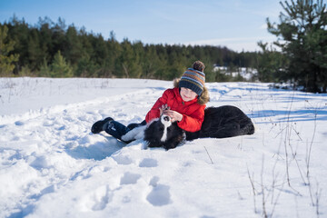 Fototapeta na wymiar Happy boy in a red jacket playing with a border collie outdoors against the backdrop of a winter forest. Love and friendship of a child and a dog. Isolation in covid19 coronavirus quarantine. 
