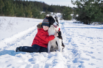 Happy boy  in a red jacket playing with a border collie outdoors against the backdrop of a winter...