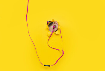 Female ear with pink vacuum headphones in a torn hole in yellow paper. The concept of a music lover, listener of music and audio relaxation. Background with copy space.