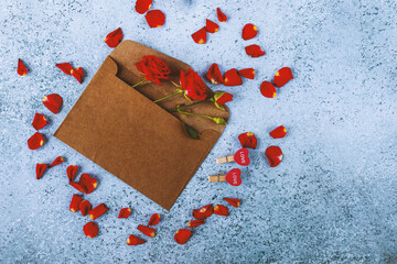 Love letter for Valentine's Day. Red roses in a brown craft envelope. Red rose petals around the envelope. Clothespins in the form of heart. Blue background.