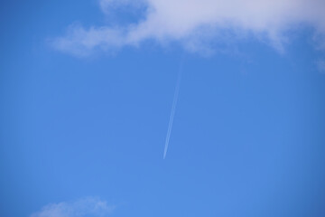 Distant passenger jet plane flying on high altitude on blue sky with white clouds leaving smoke trace of contrail behind. Air traveling concept