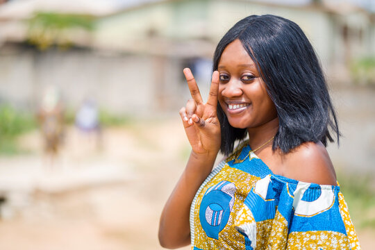 close up image of beautiful african lady with two fingers up, cheerful black woman out door