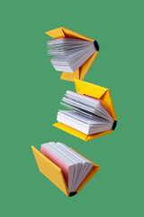 miniature books in a yellow cover fly on a green background